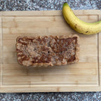 Loaf of bread and banana on a wooden cutting board with a gray countertop background